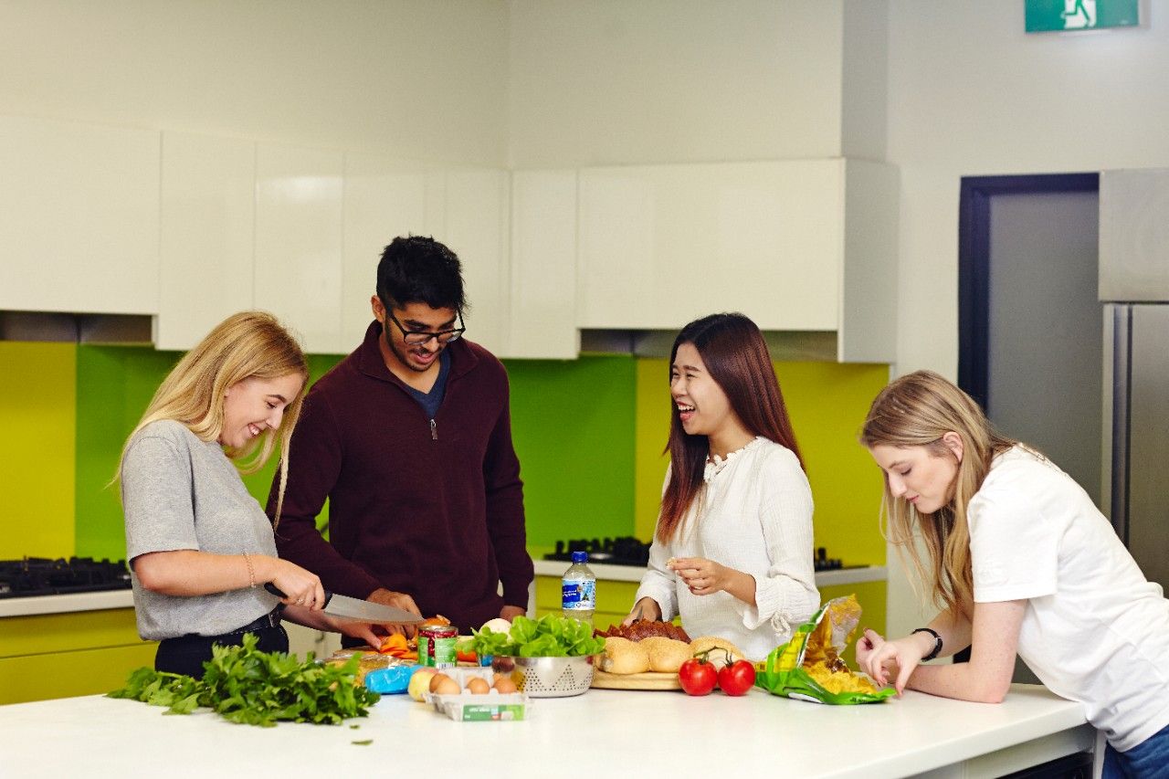Four happy students in a test kitchen prepare a range of healthy food.