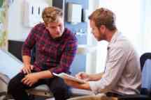 Male patient and doctor have consultation in hospital room.