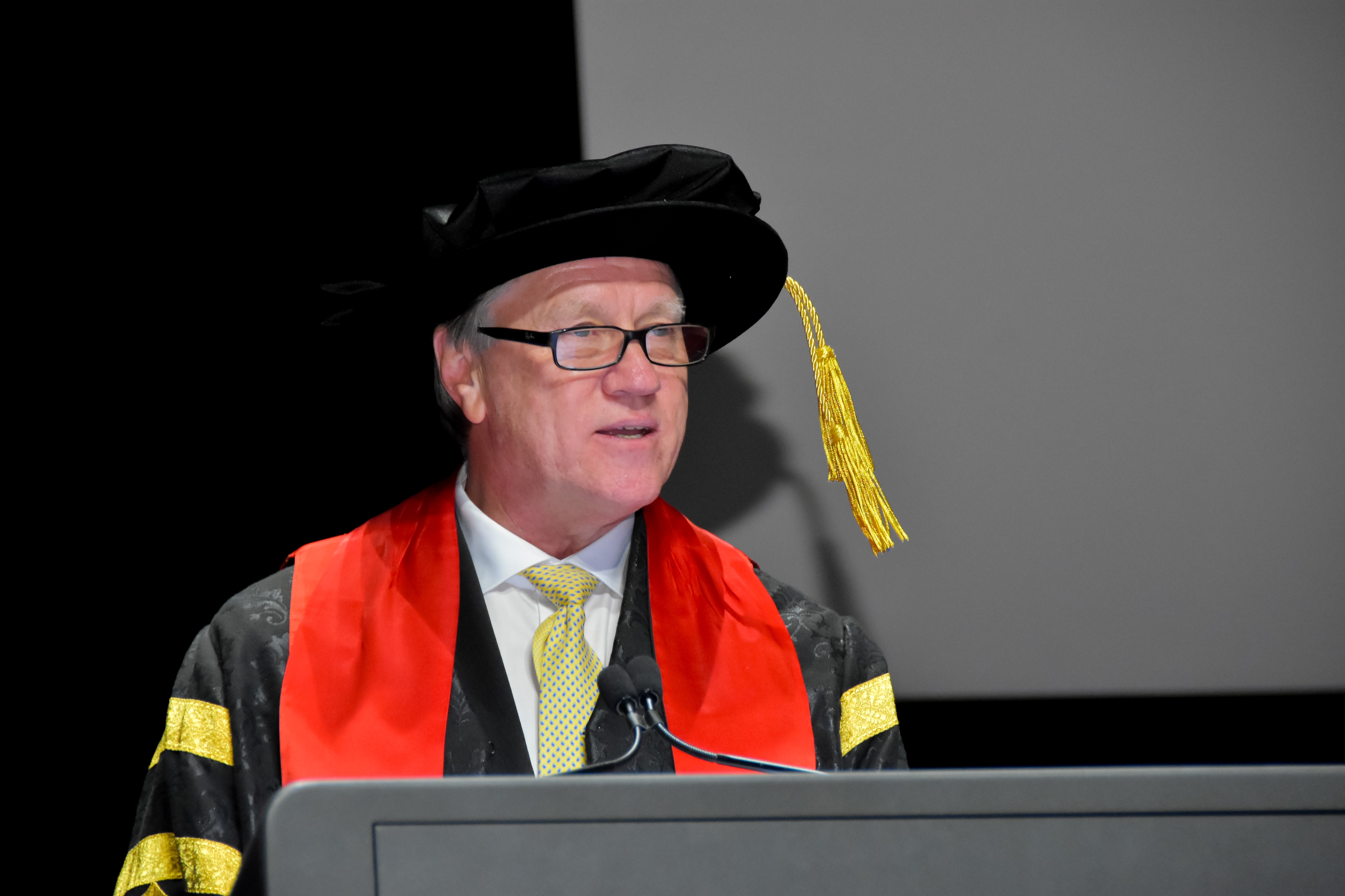 chancellor standing behind a podium in academic dress giving a speech