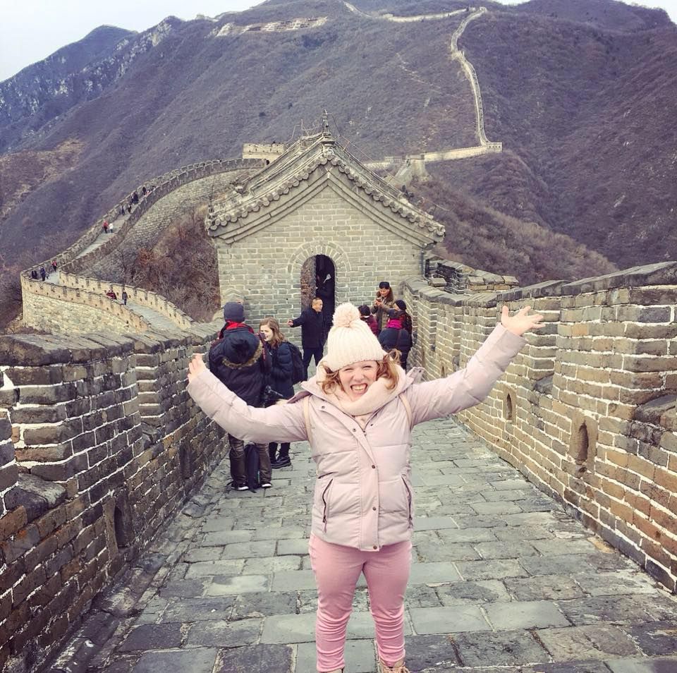 Female student in pink smiling at the camera while on the Great Wall of China