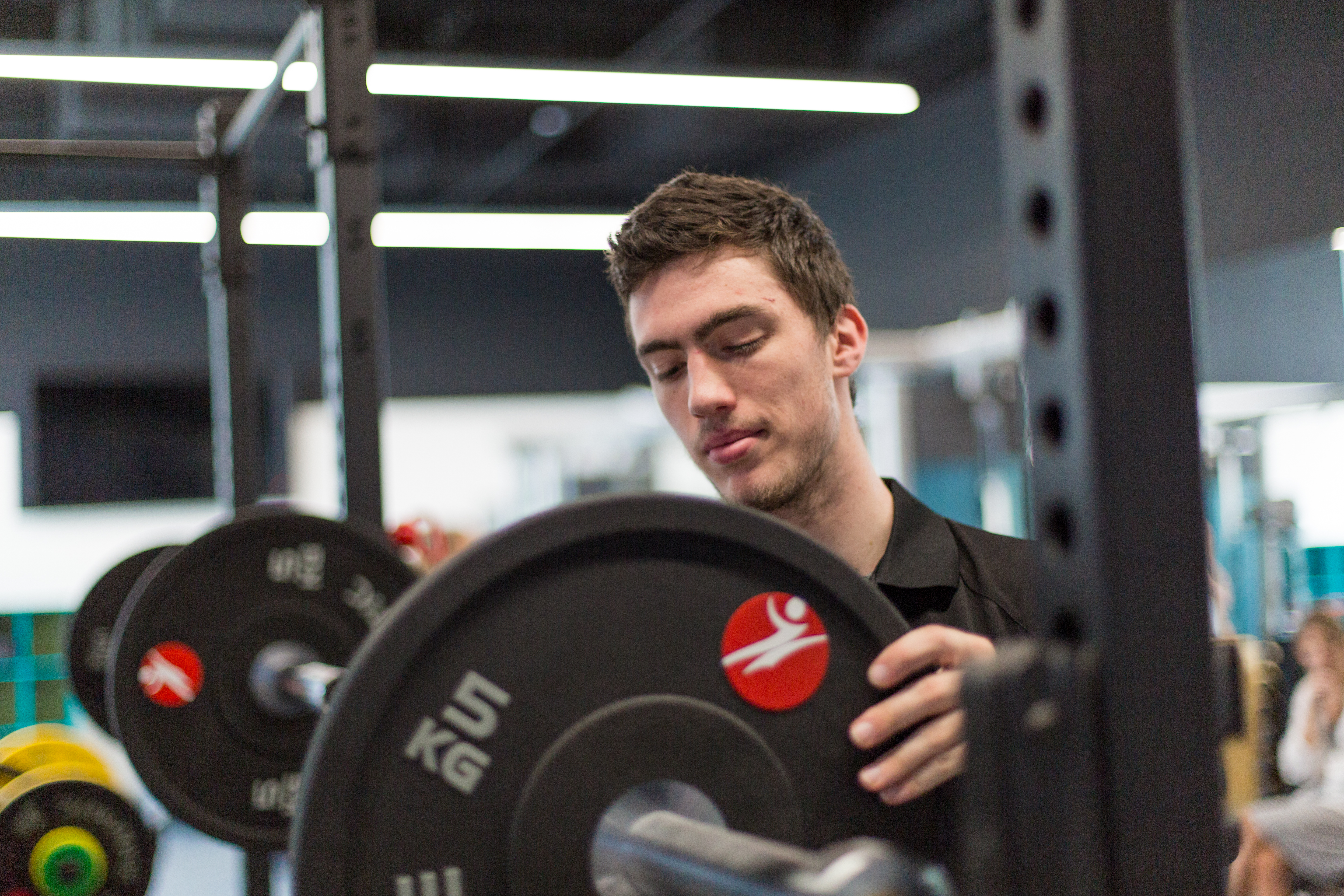Male student in the gym lifts a weight onto a bar