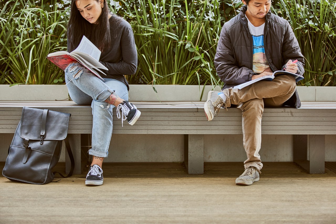 Two students enjoy the outdoor spaces of Swinburne’s Hawthorn campus as they read course texts.