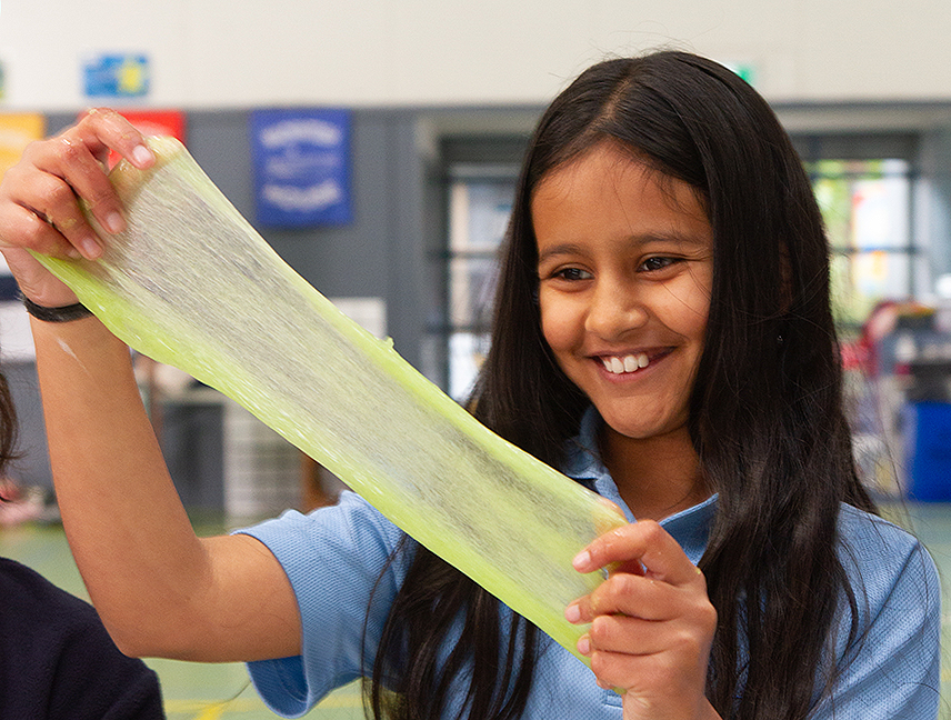 Young school girl is smiling while stretching green slime