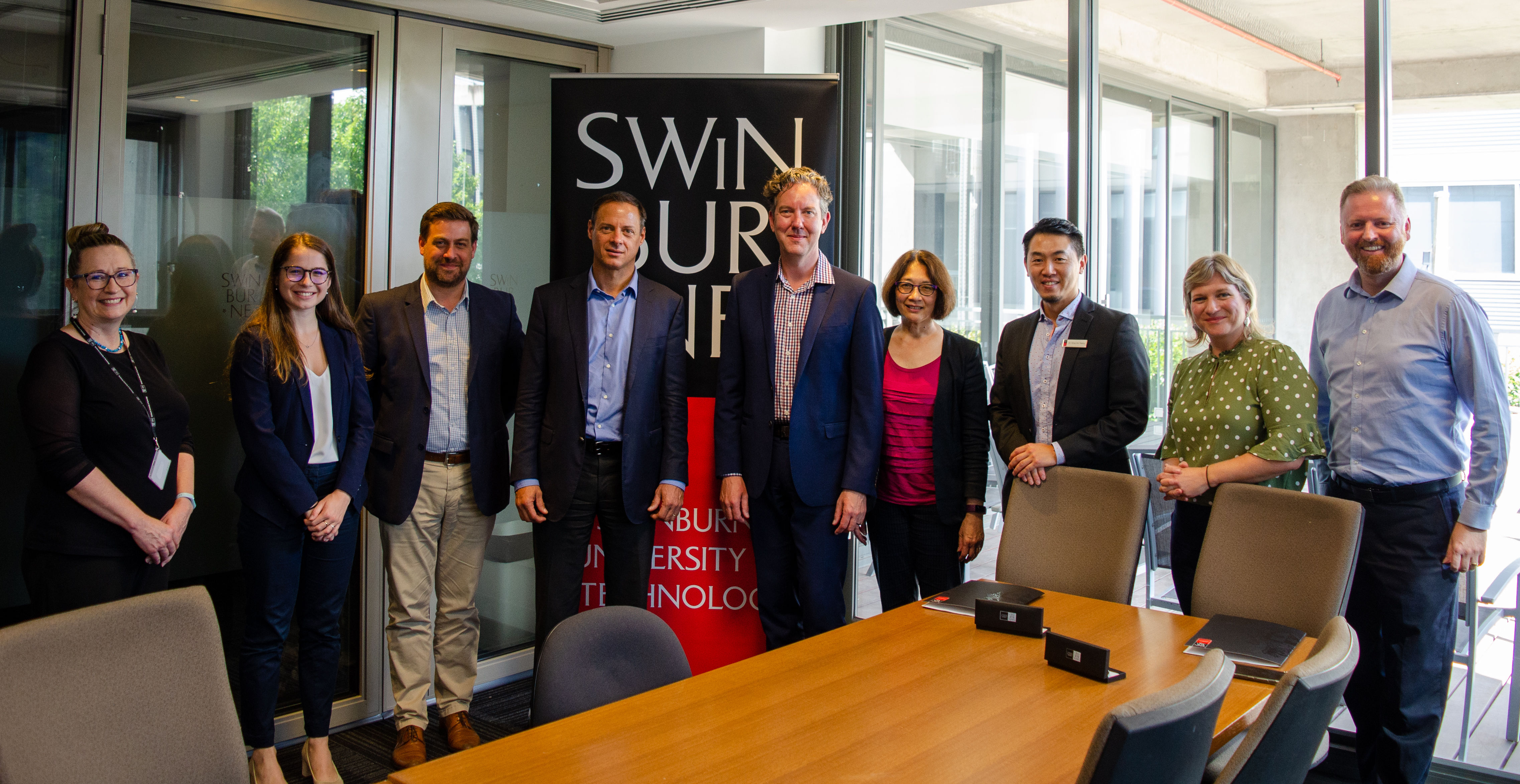 Representatives from Swinburne and BYCA standing behind a Swinburne banner in a meeting room. 