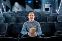 Young man sits in an empty cinema with a bucket of Lido popcorn.