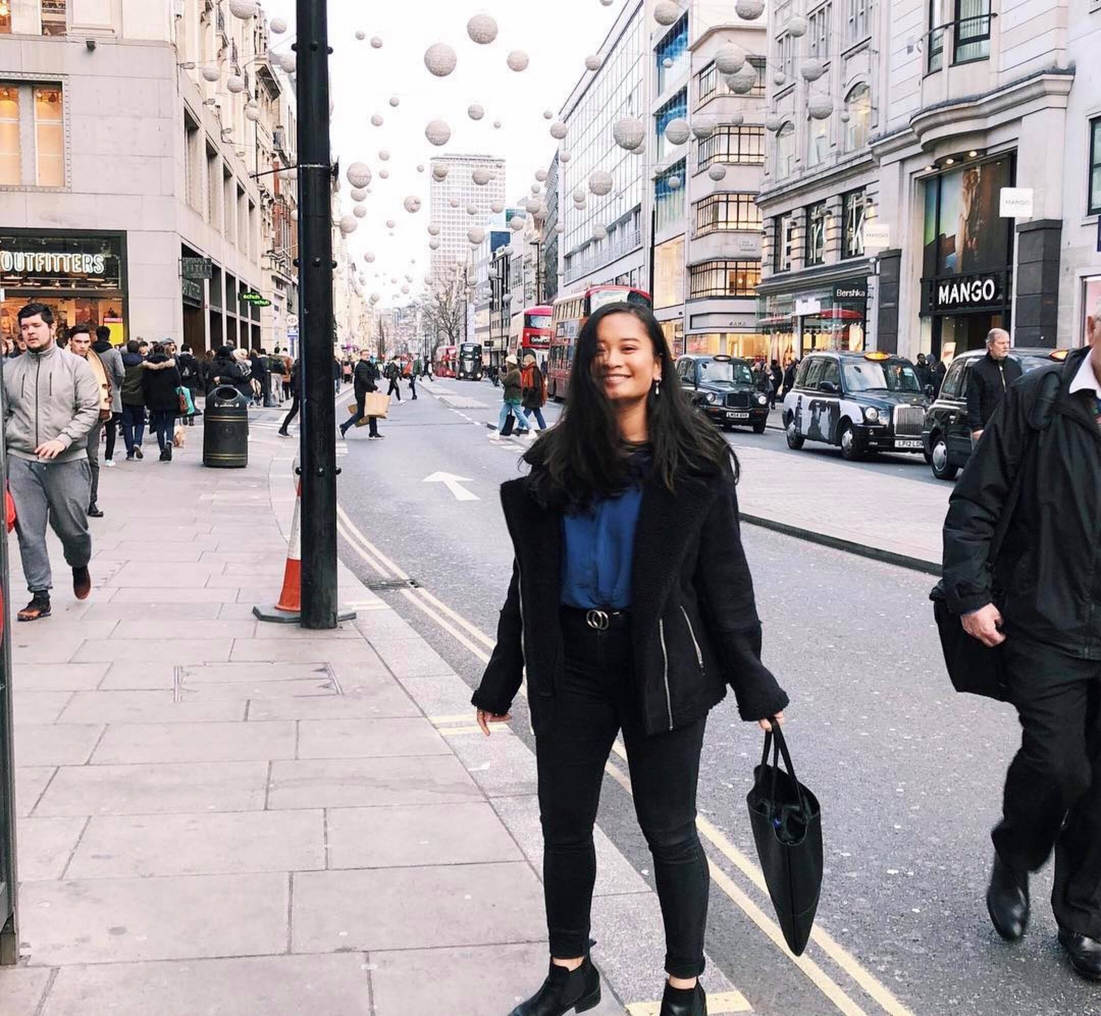 Study abroad student wearing black pants and jacket, smiling at the camera on a busy London street