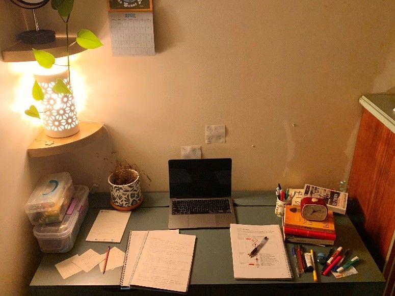 Ingrid’s desk, warmly lit and with scattered study materials, a pot plant and a stack of novels.