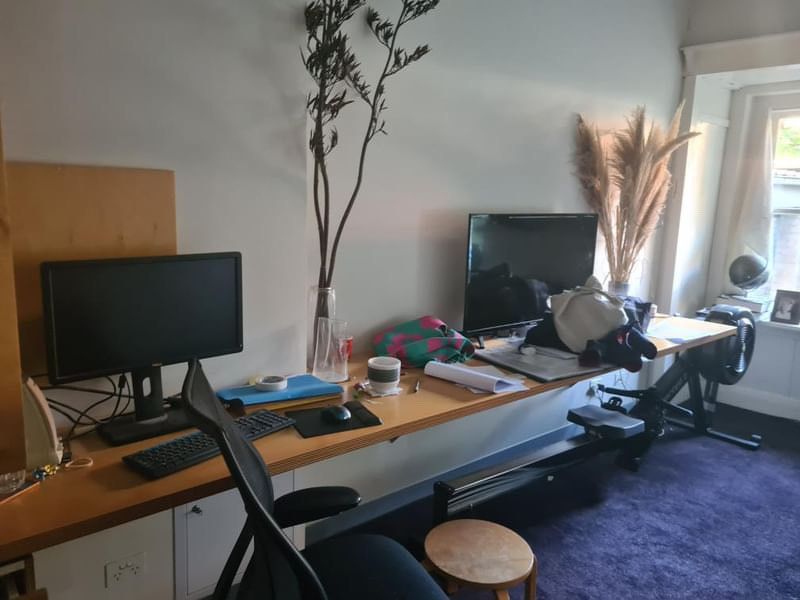 Poppy’s shared desk in her family home with two computers, a pile of clothes, various stationery and a rowing machine tucked underneath.