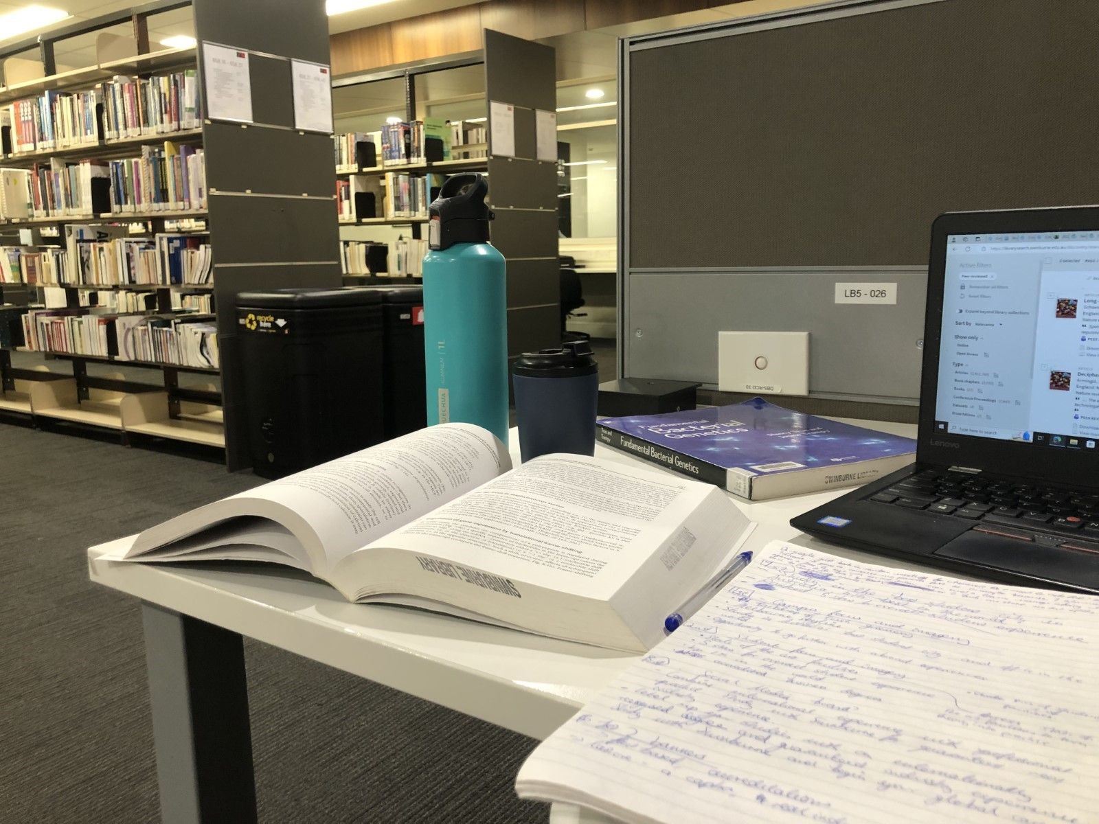 A desk in the Swinburne library with a laptop, open textbooks and a water bottle.